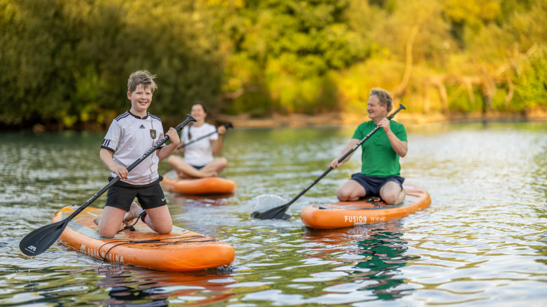 Kind, Mutter und Vater vergnügen sich beim Stand-Up-Paddling auf der Fulda.