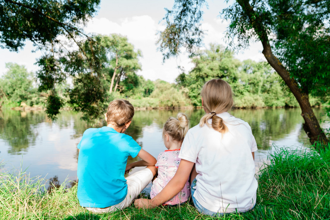 Three children sit on the banks of the Fulda at the Kassel campsite and enjoy the view